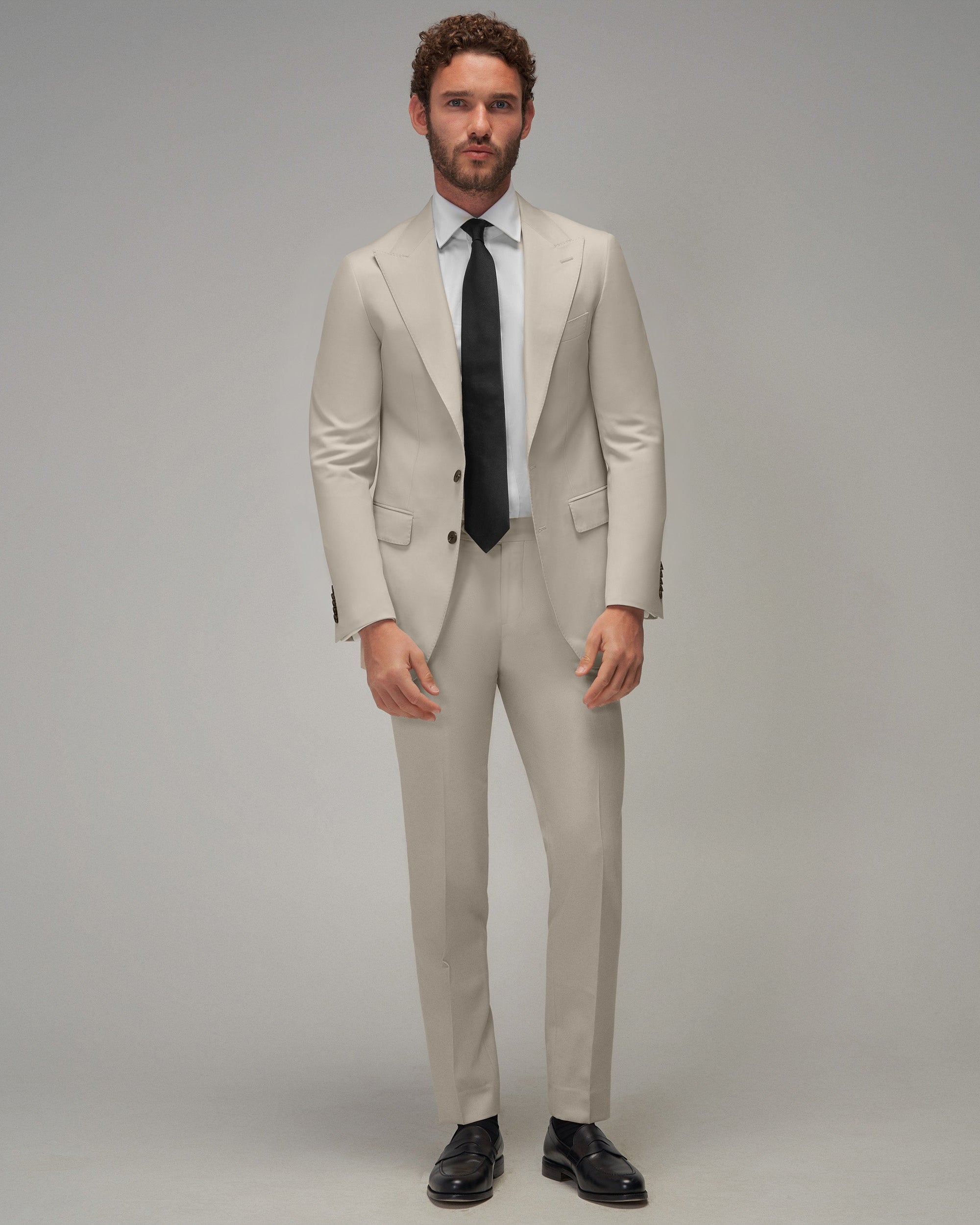 Man wearing a beige suit with a black tie on a gray background