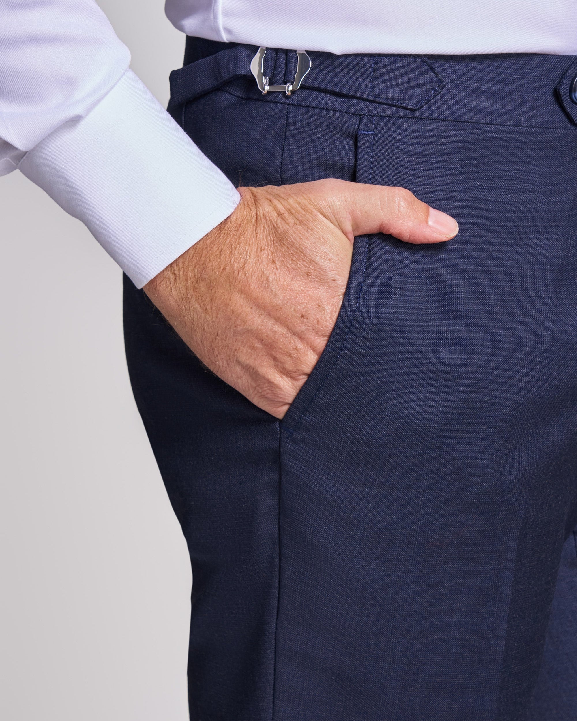 Navy blue dress pants with a white shirt cuff and belt buckle on a light gray background