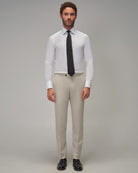 Man wearing a white dress shirt, black tie, beige pants, and black shoes on a gray background