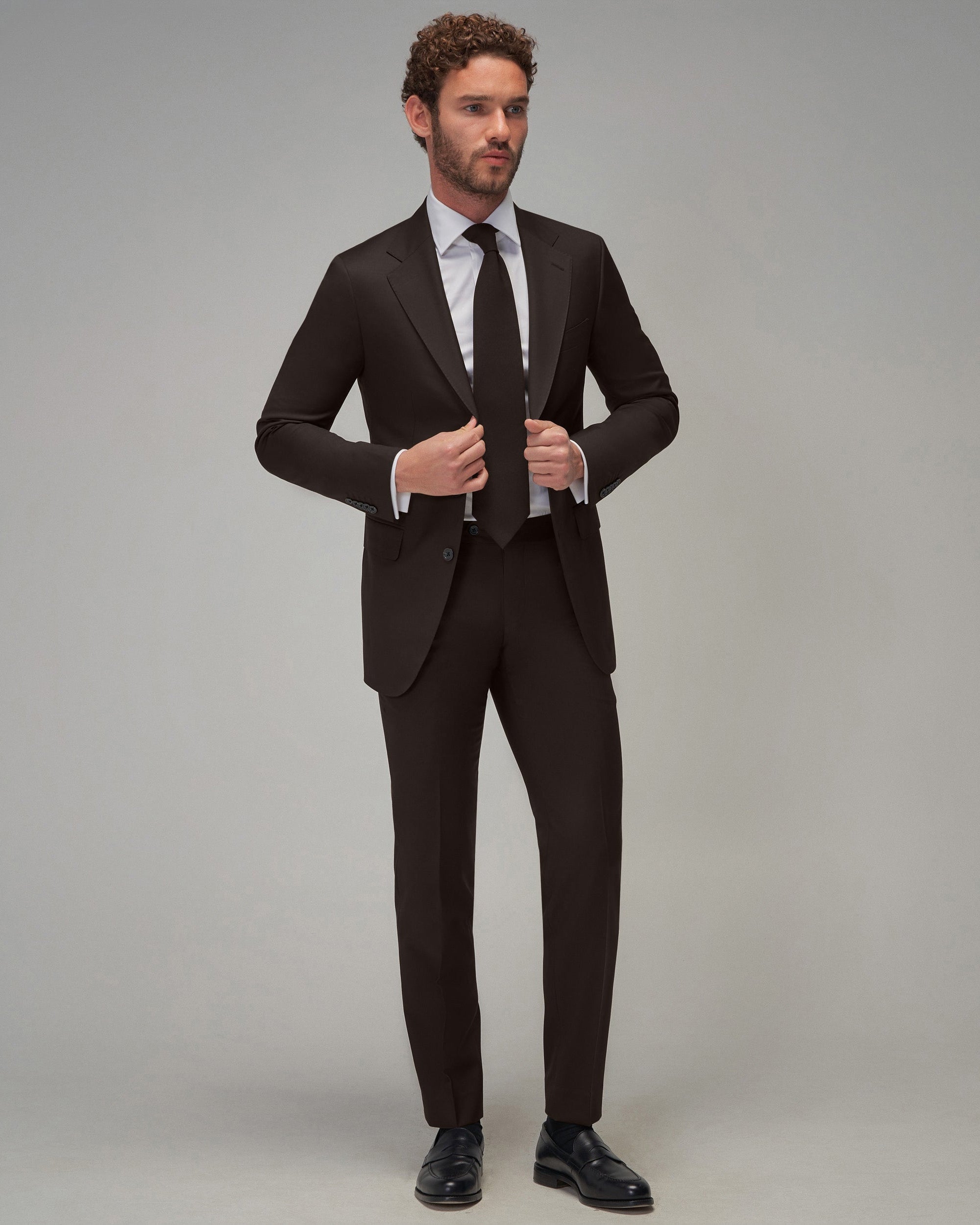 Man wearing a black suit with a white shirt and black tie on a gray background