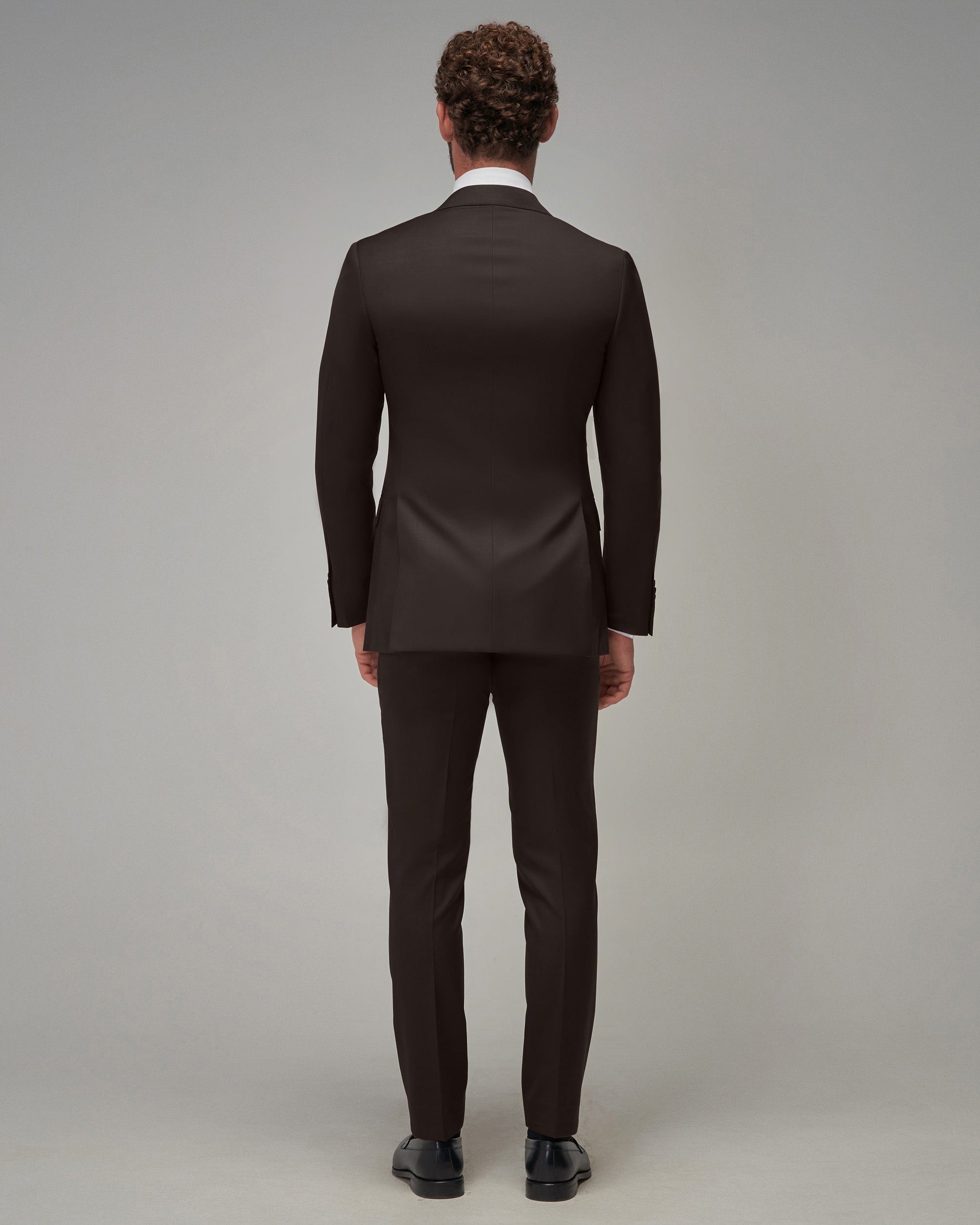 Man wearing a brown suit standing against a plain background