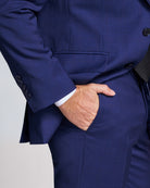 Close-up of a person wearing a blue suit with one hand in the pocket against a light gray background